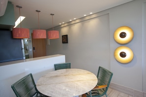 Uma sala de jantar moderna com uma mesa redonda de mármore, cadeiras verdes e luminárias pendentes.