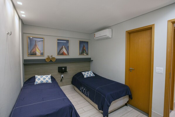 A room with two beds, a wooden door, and three framed pictures on the wall. - Flat de Luxo em Muro Alto (Porto de Galinhas Ipojuca)