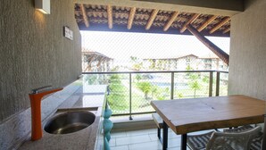 Un balcone con tavolo e sedie, un lavandino e vista su un edificio e vegetazione.