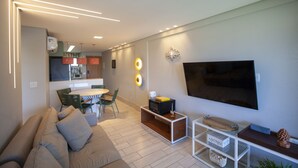Un soggiorno moderno con un divano, un tavolino, una TV e un angolo cottura sullo sfondo.