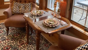 Ein gemütliches Zimmer mit einem karierten Sessel, einem Esstisch mit Tellern und Besteck sowie einer Lampe.