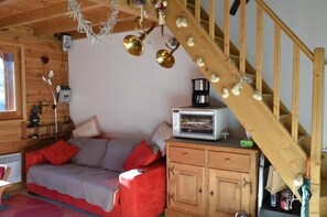 Een gezellige kamer met een houten trap, een bank met rode kussens, een klein kastje en een magnetron erop.