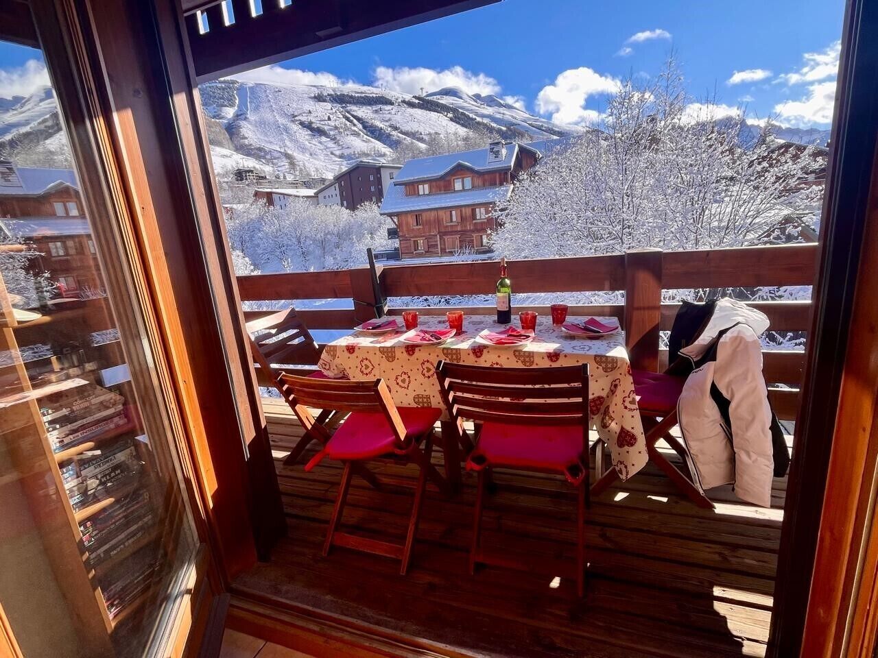 Un coin repas avec une table dressée pour deux personnes, des chaises en bois et une vue sur des montagnes enneigées.