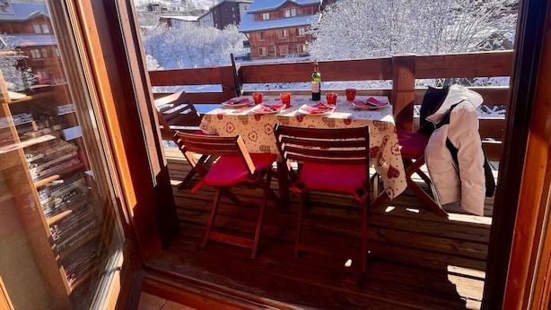 A dining area with a table set for two, wooden chairs, and a view of snow-covered mountains. - Appartement Plein Sud (Les Deux Alpes)