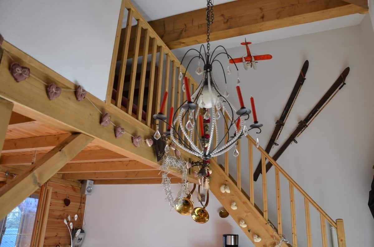 Eine Holztreppe mit einer Chandelüster und Skiausrüstung an der Wand.