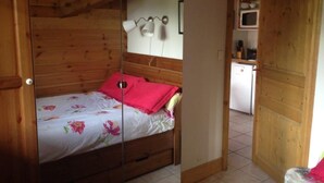 A wooden room with a bed, a small kitchenette, and a door. - Appartement Plein Sud (Les Deux Alpes)