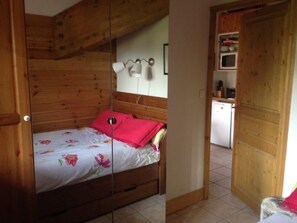 Een houten kamer met een bed, een klein keukentje en een deur.