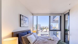 A modern bedroom with a large bed, a bedside lamp, and a city view through a sliding glass door. - Toowong Central, Carpark+Wifi, Great value 1BR Apt (Toowong)