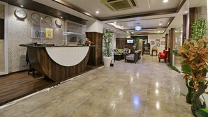 Zona de recepción de hotel con un mostrador de madera, relojes y una pantalla de televisión.