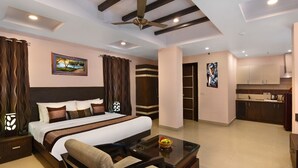 Habitación de hotel con una cama grande, una zona de estar con una mesa de centro, un ventilador de techo, un cuadro y una kitchenette.