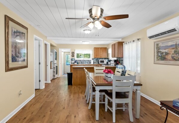 A kitchen with wooden cabinets, a dining table with chairs, a ceiling fan, and a window.