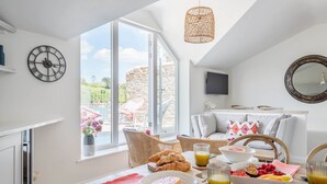 A bright kitchen with a breakfast setup, including croissants, fruit, and juice, and a view of the outdoors. - The Old Lobster Pot -  a beautiful, luxury waterfront cottage in the centre of Salome (Salcombe)