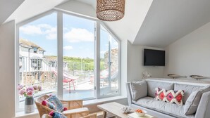 A spacious living room with large windows, a comfortable sofa, a wicker chair, and a wooden coffee table. - The Old Lobster Pot -  a beautiful, luxury waterfront cottage in the centre of Salome (Salcombe)