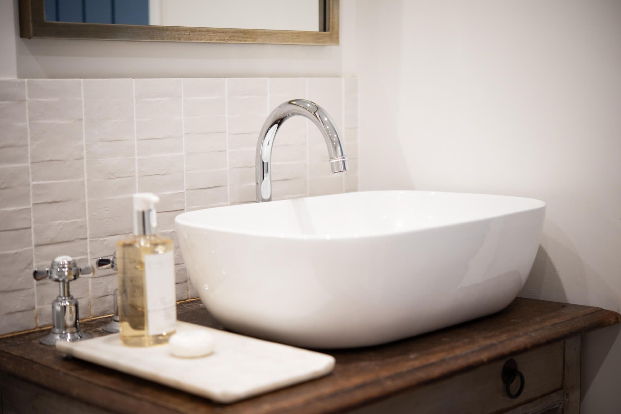 Une salle de bain avec un lavabo blanc, un miroir au-dessus et un plan de travail en bois.