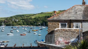 A stone building with a stone roof, a small balcony with metal railings, and a view of a harbor with various boats. - The Old Lobster Pot -  a beautiful, luxury waterfront cottage in the centre of Salome (Salcombe)