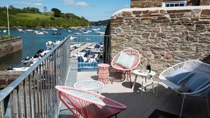 A balcony with wicker chairs, a small table, and a bottle of champagne. A stone wall and a view of boats on the water are visible. - The Old Lobster Pot -  a beautiful, luxury waterfront cottage in the centre of Salome (Salcombe)