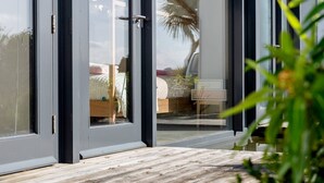 A modern outdoor area with a wooden deck, a water feature, and a view of a bedroom with a bed and a nightstand. - Quarry House -  An architecturally inspiring house with sea views (West Charleton)