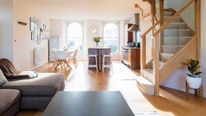 Ein modernes Wohnzimmer mit Sofa, Couchtisch und Essbereich mit Stühlen und Tisch. Eine Treppe führt zu einer oberen Ebene.