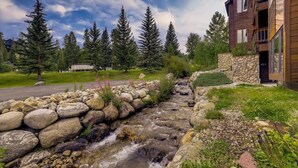 A stone-lined stream, wooden cabin, and a modern building with a stone wall and balcony. - Lift View Place | Steps to Lift | Walk to Main St! (Breckenridge)