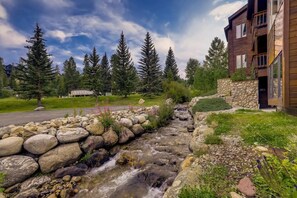 A stone-lined stream, wooden cabin, and a modern building with a stone wall and balcony.