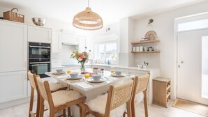 Cozinha moderna com armários brancos, uma mesa de jantar para quatro pessoas e uma luminária pendente de vime.