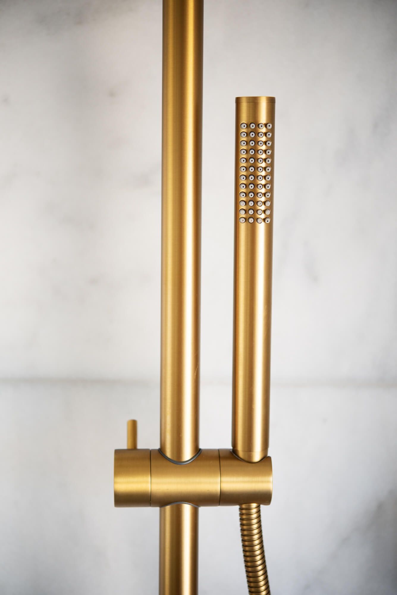 Un cabezal de ducha dorado con una manguera flexible conectada a un accesorio montado en la pared.