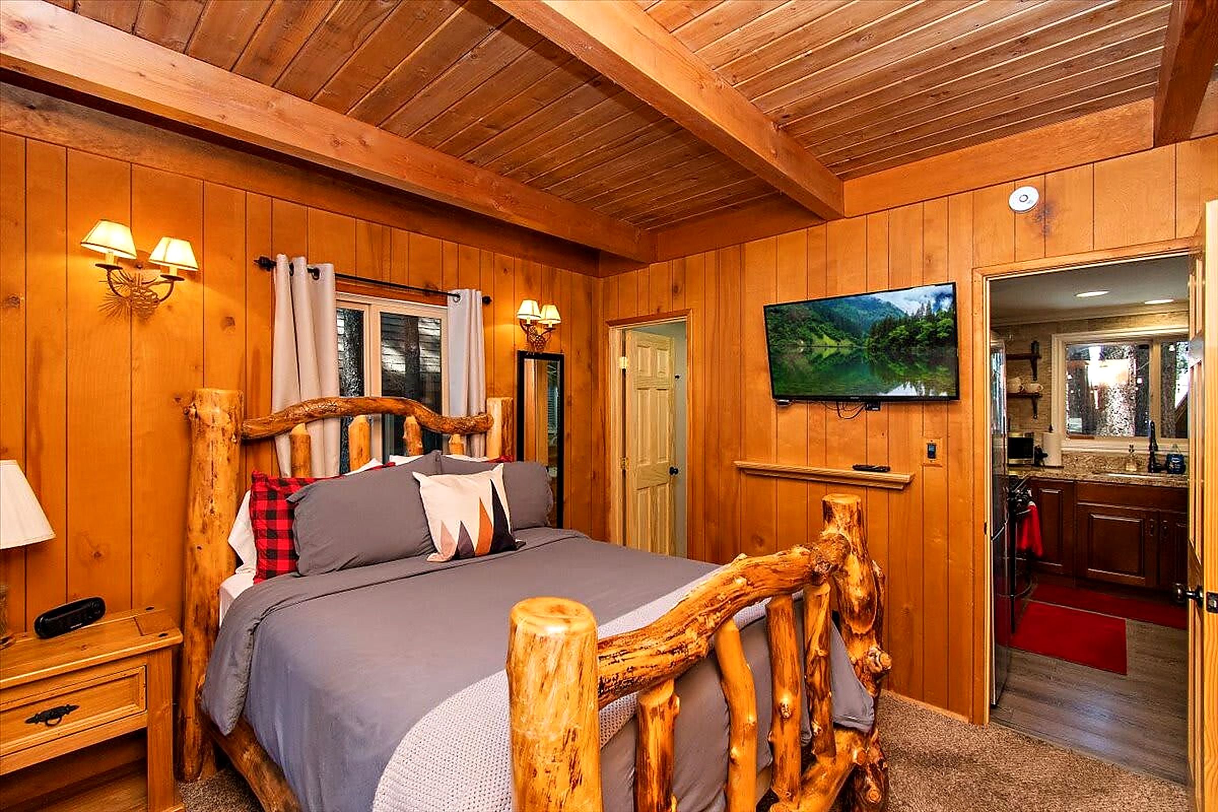 Una habitación de madera con una cama, un televisor y una puerta que da a un baño.