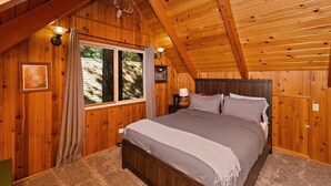 Ein Schlafzimmer mit Holzboden, einem Bett, einem Nachttisch, einem Fenster mit Vorhängen und einem an der Wand befestigten Hirsch-Dekoration.