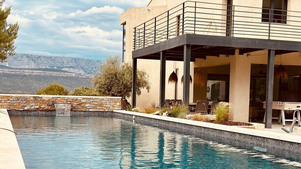 Piscina moderna con pared de piedra y vista a las montañas.