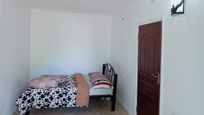 A narrow hallway with a bed on the left and a door on the right. - Naivasha Homestay (Naivasha)