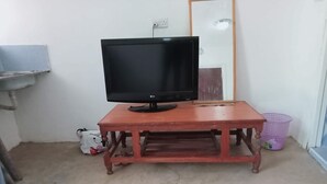A room with a wooden table, a black LG TV, a white bag, a purple laundry basket, and a mirror on the wall. - Naivasha Homestay (Naivasha)