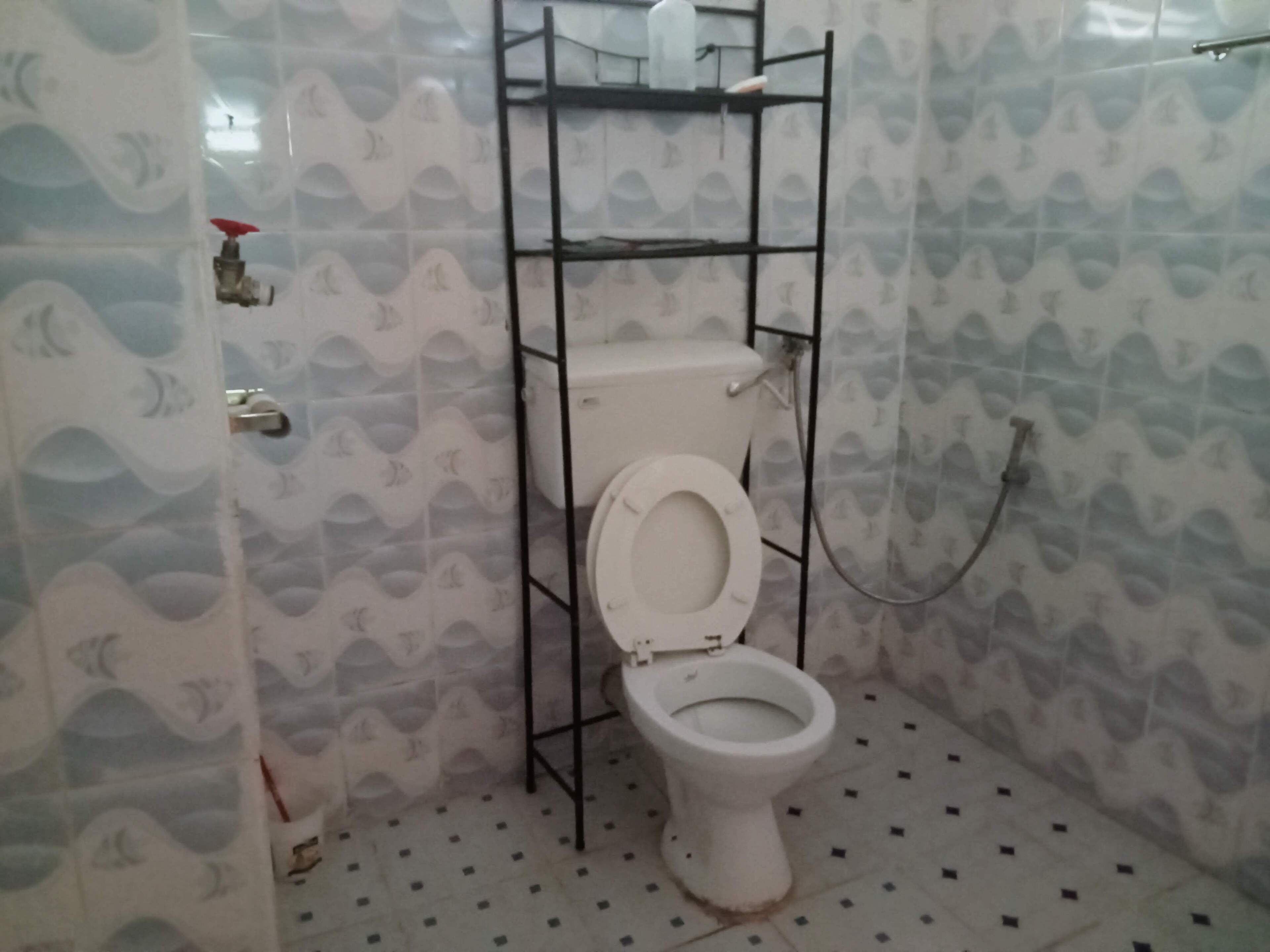 Casa de banho com sanita montada numa estrutura de metal preto, paredes revestidas a azulejo com padrão de ondas e chão em mosaico com pequenos azulejos quadrados.