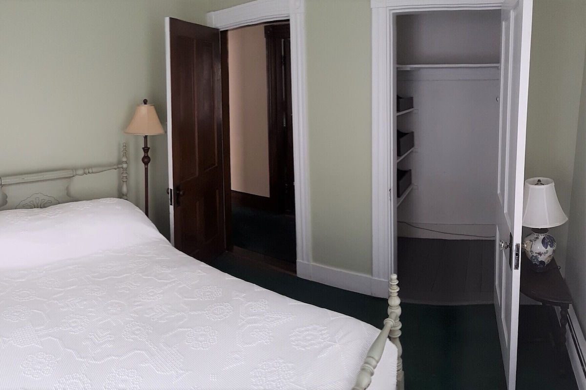 A single bed with a wooden headboard, a bedside lamp, and a wardrobe with a mirror.