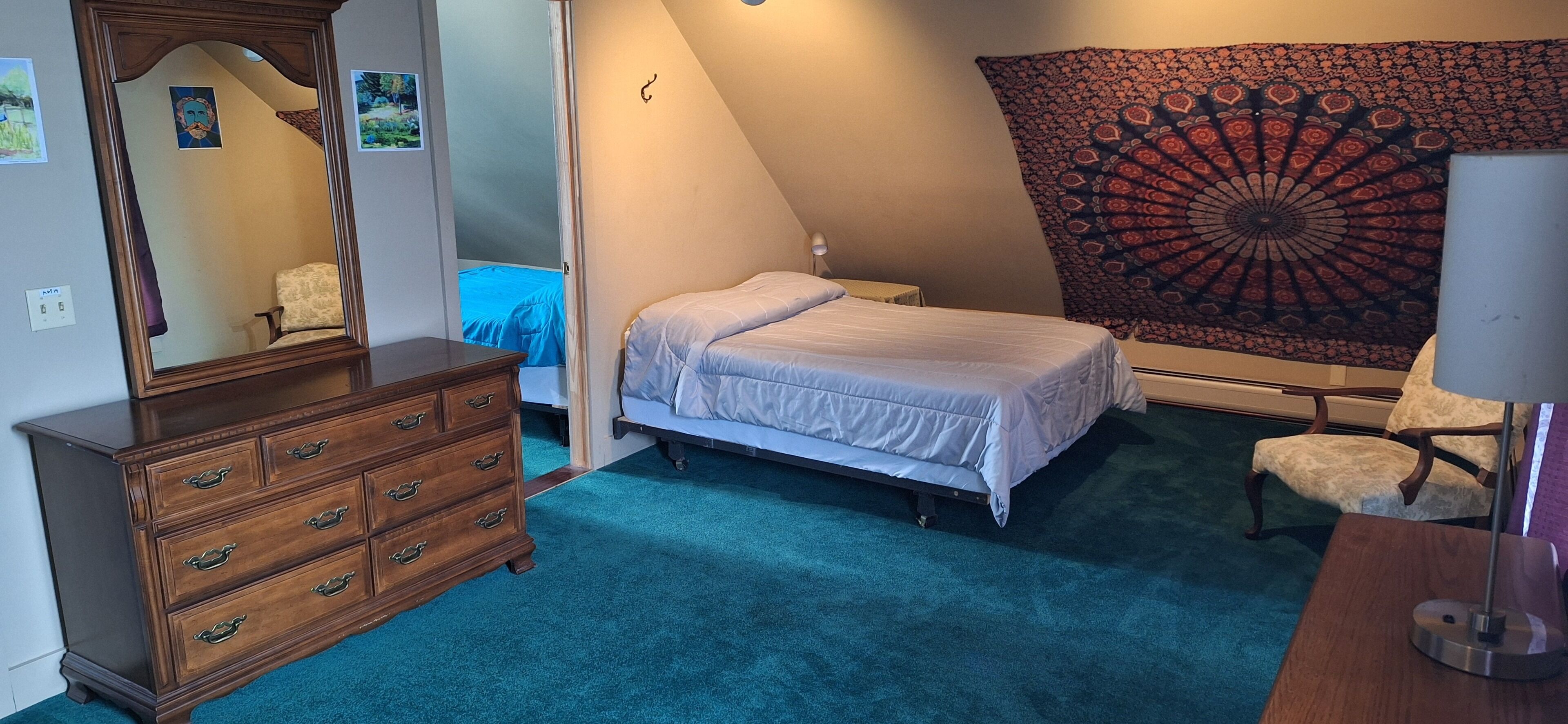 A bedroom with a bed, dresser, chair, and tapestry.