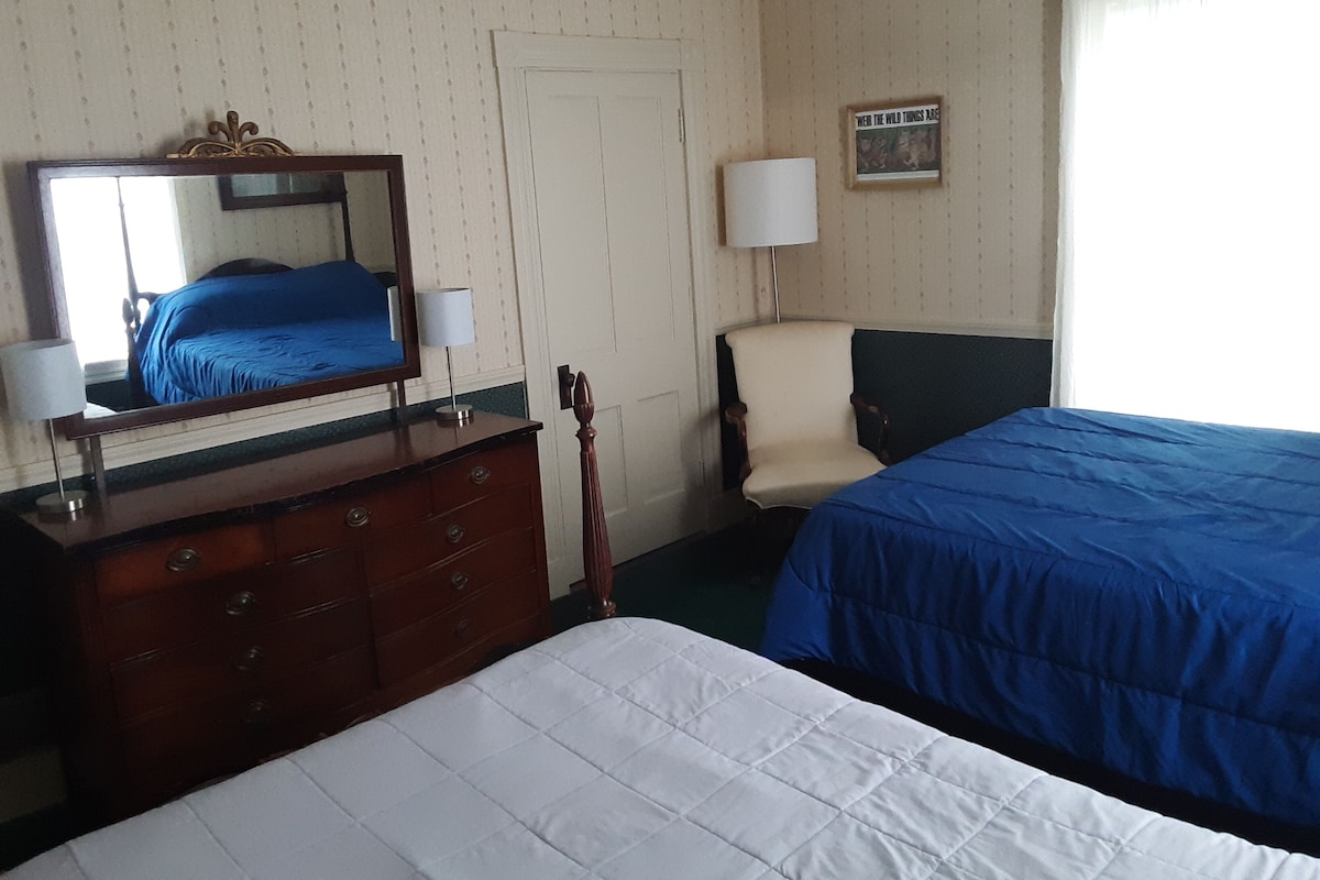 A hotel room with a bed, a dresser, a chair, a mirror, and a window with curtains.