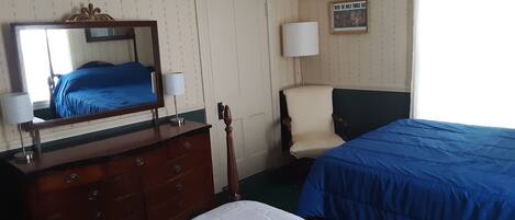 A hotel room with a bed, a dresser, a chair, a mirror, and a window with curtains.