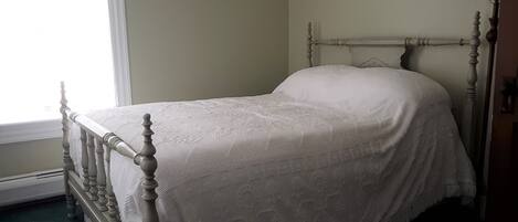 A bed with a wooden frame and a white bedspread in a room with a window and a lamp.