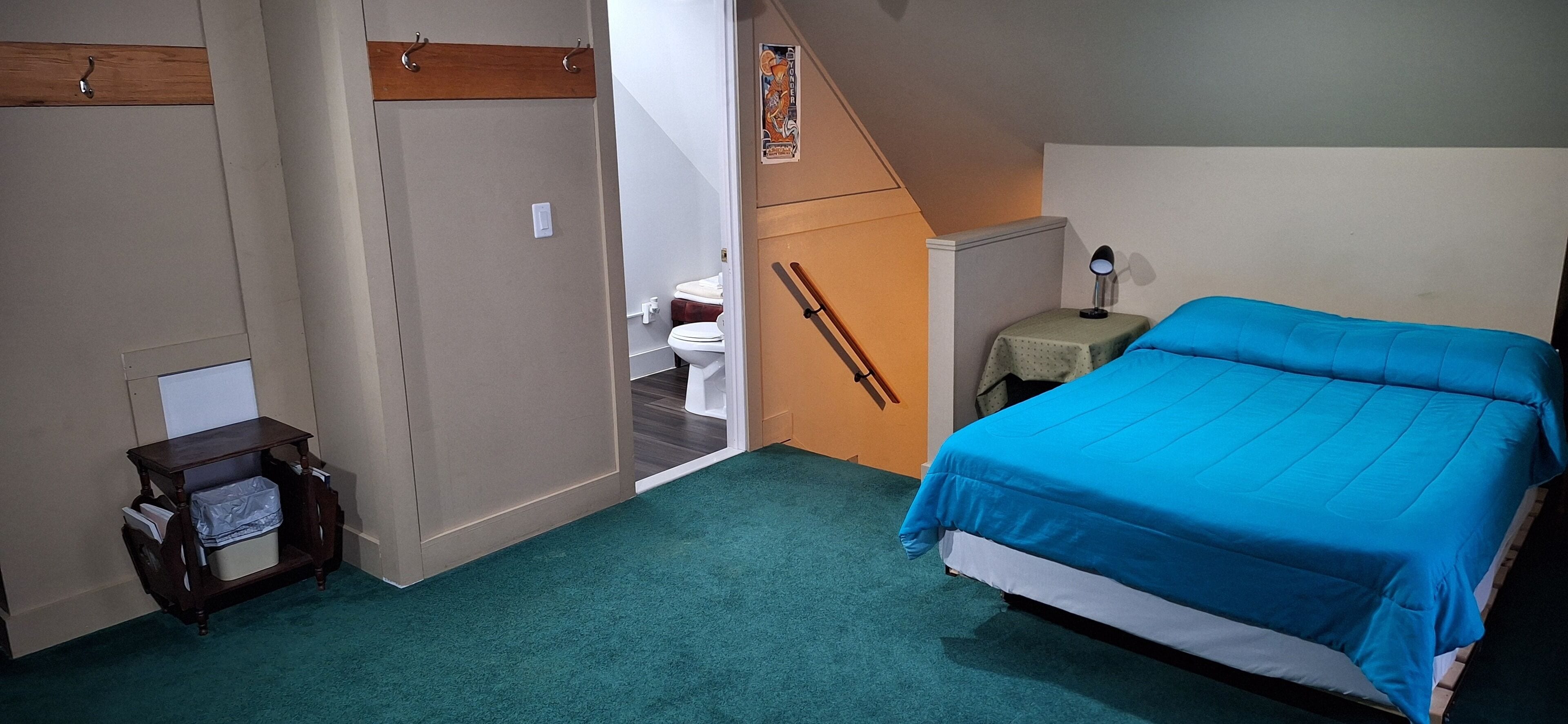 A bedroom with a bed, a nightstand, a desk, a chair, a toilet, and a staircase.