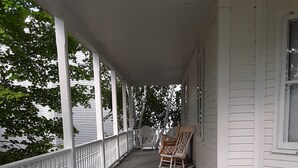 A covered porch with white railings and two wicker chairs. - Terrapin Hostel (Kingfield)