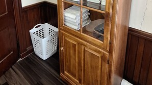 A corner room with a wooden cabinet with glass doors, a white laundry basket, and a radiator on the floor. - Terrapin Hostel (Kingfield)