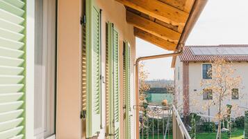 Una casa con persiane verdi, un balcone in legno e vista sulle case e gli alberi vicini.