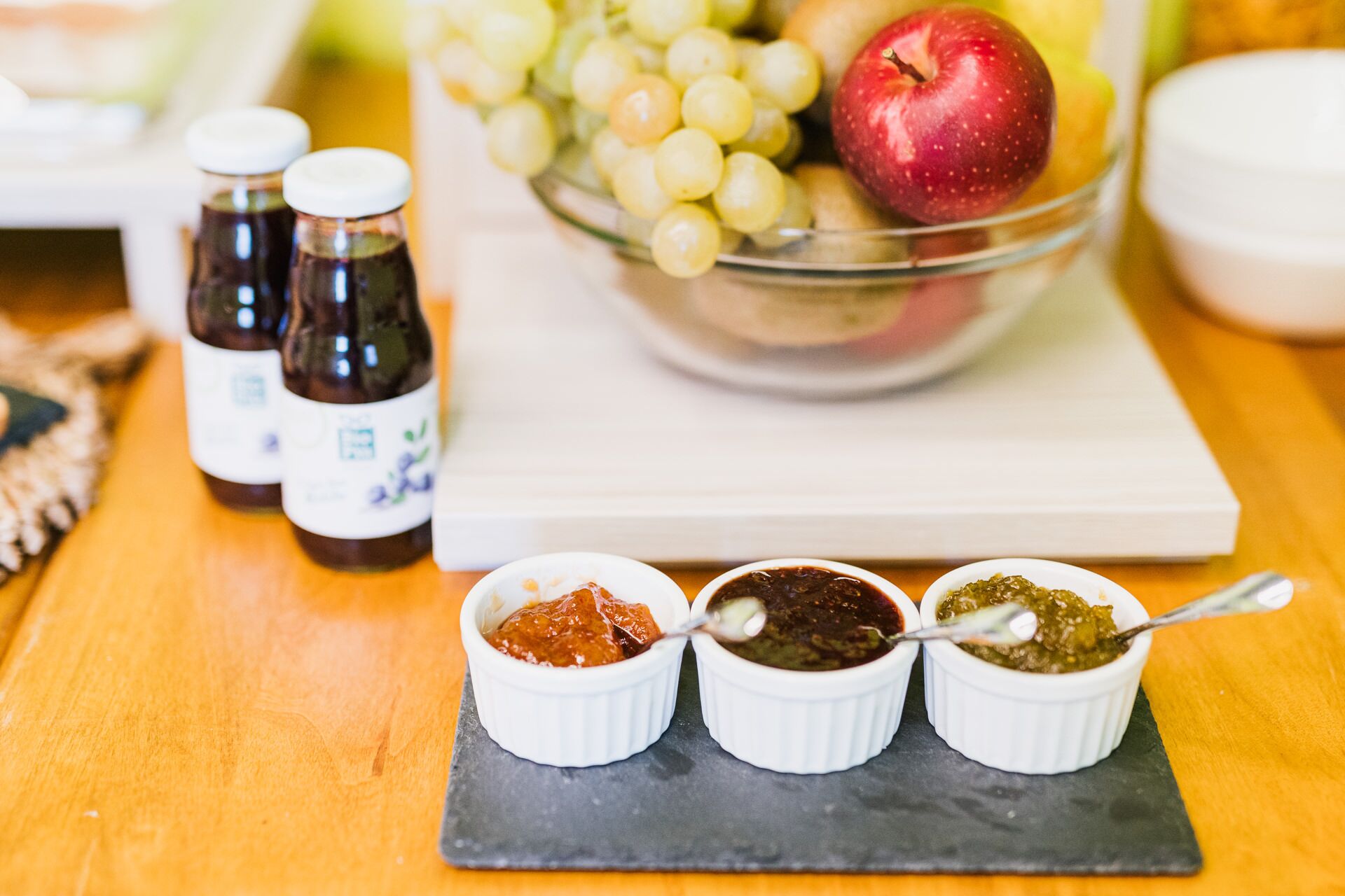 Uma mesa com uma tigela de frutas, três pequenas tigelas de acompanhamentos e duas garrafas de molho.