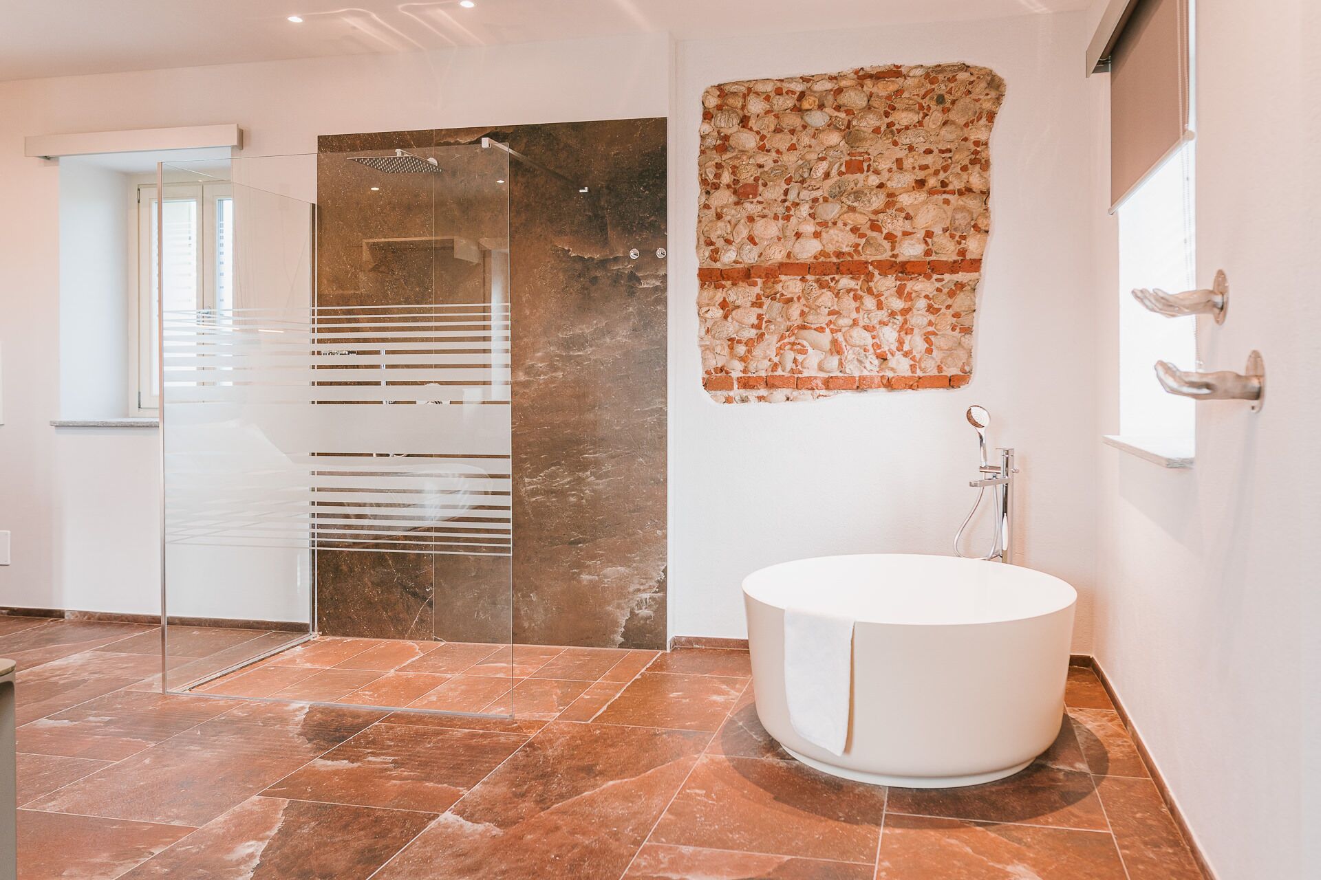 Une salle de bain moderne avec une douche à l’italienne en verre, un mur décoré d’une mosaïque de pierre et une baignoire blanche.