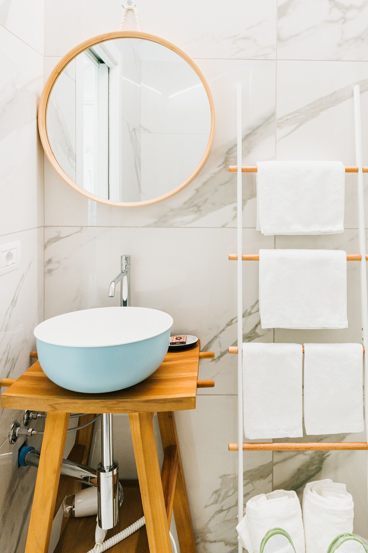A bathroom with a round mirror, a blue sink, and a towel rack with multiple white towels.