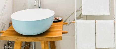 A bathroom with a round mirror, a blue sink, and a towel rack with multiple white towels.