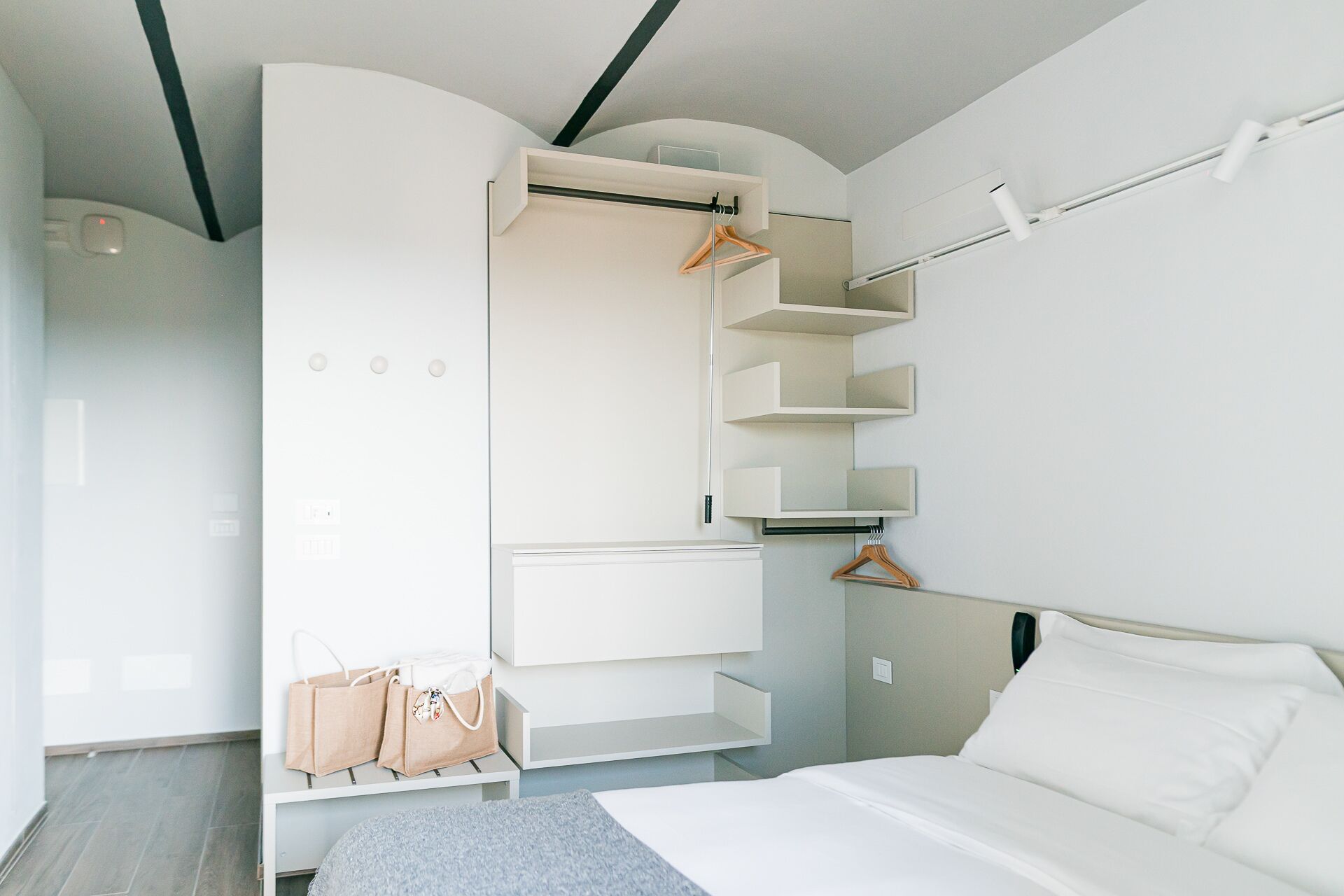 A bedroom with a bed, a wardrobe with hanging space, and a bedside table with a bag.