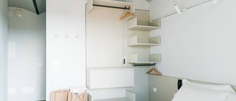 A bedroom with a bed, a wardrobe with hanging space, and a bedside table with a bag.