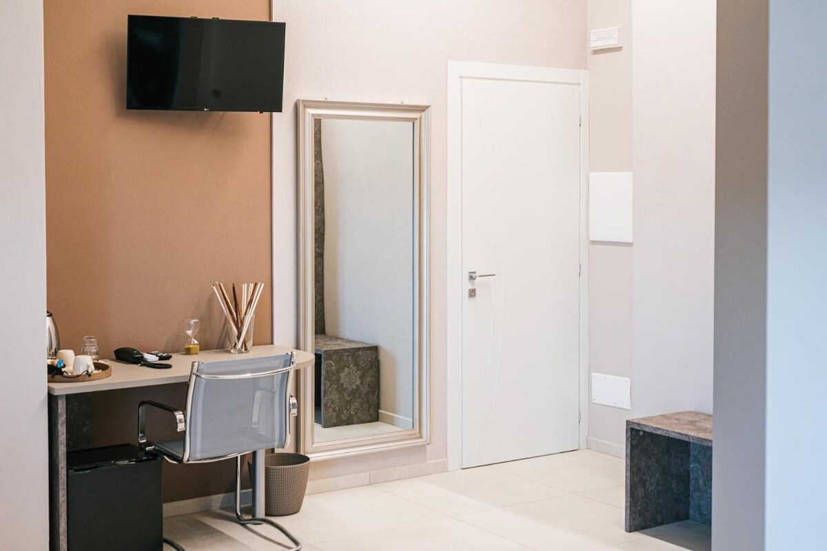 Une chambre d’hôtel équipée d’un bureau, d’une chaise, d’une télévision, d’un miroir et d’une porte.