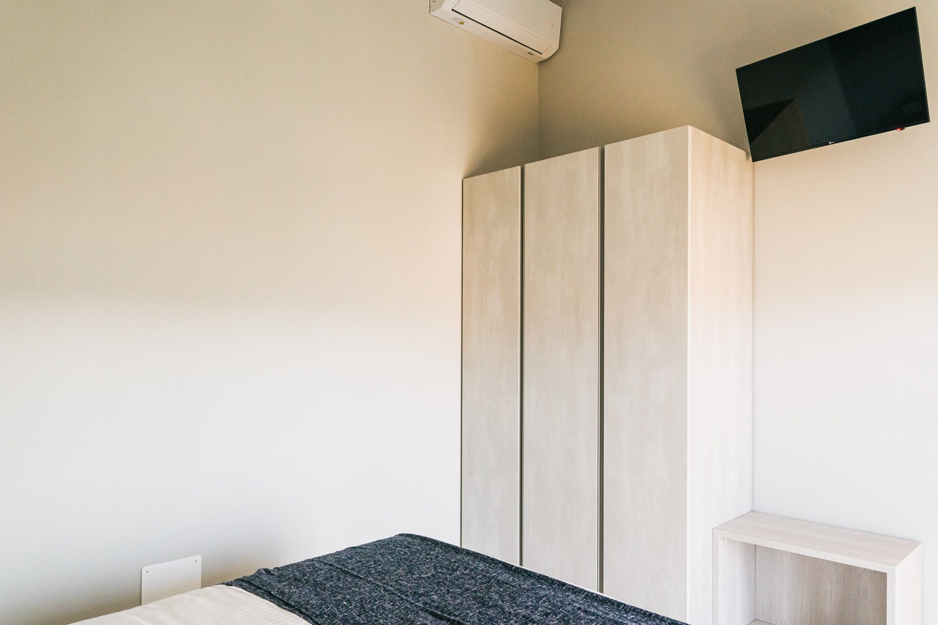 A bedroom with a bed, a wardrobe, and a TV mounted on the wall.