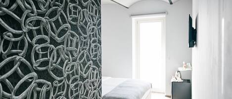 A modern bedroom with a bed, a bedside table, and a large window.